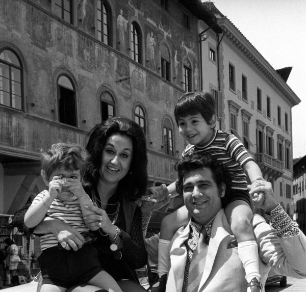 Mexican soprano Marta Ornelas holding her son Alvaro Domingo with a toy camera in the hands in front of Palazzo dell'Antella on piazza Santa Croce. Beside her, her Spanish husband and tenor Placido Domingo smiling while carrying piggyback their son and Mexican singer Placido Domingo Jr. Florence, 1970s