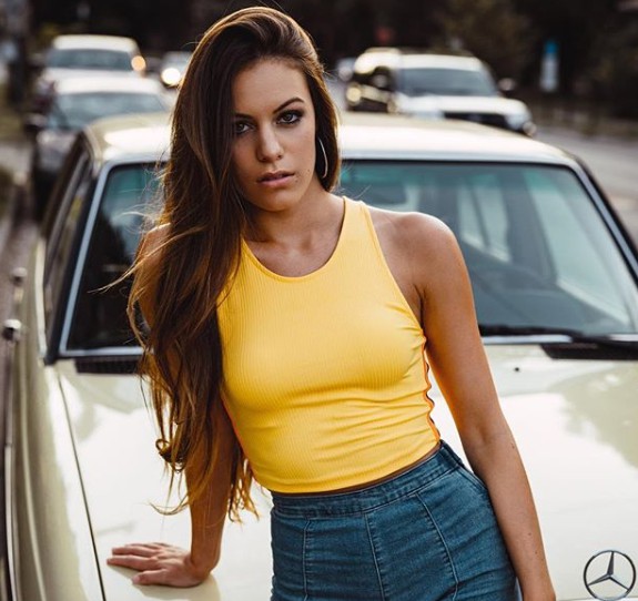 Taylor Monaco posing for a photowhile placing her hand on car 
