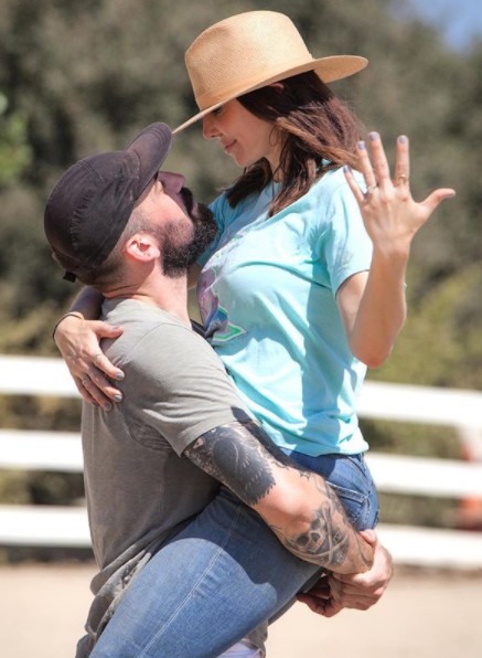 Whitney Cummings showing her engagement ring while carried by her partner Miles