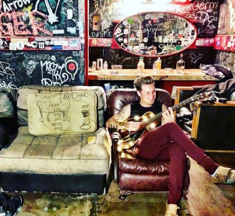 Ryan Cabrera sitting on sofa and plying guitar