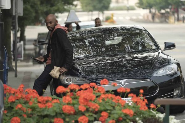 Romany Malco posing for a photo with a car 